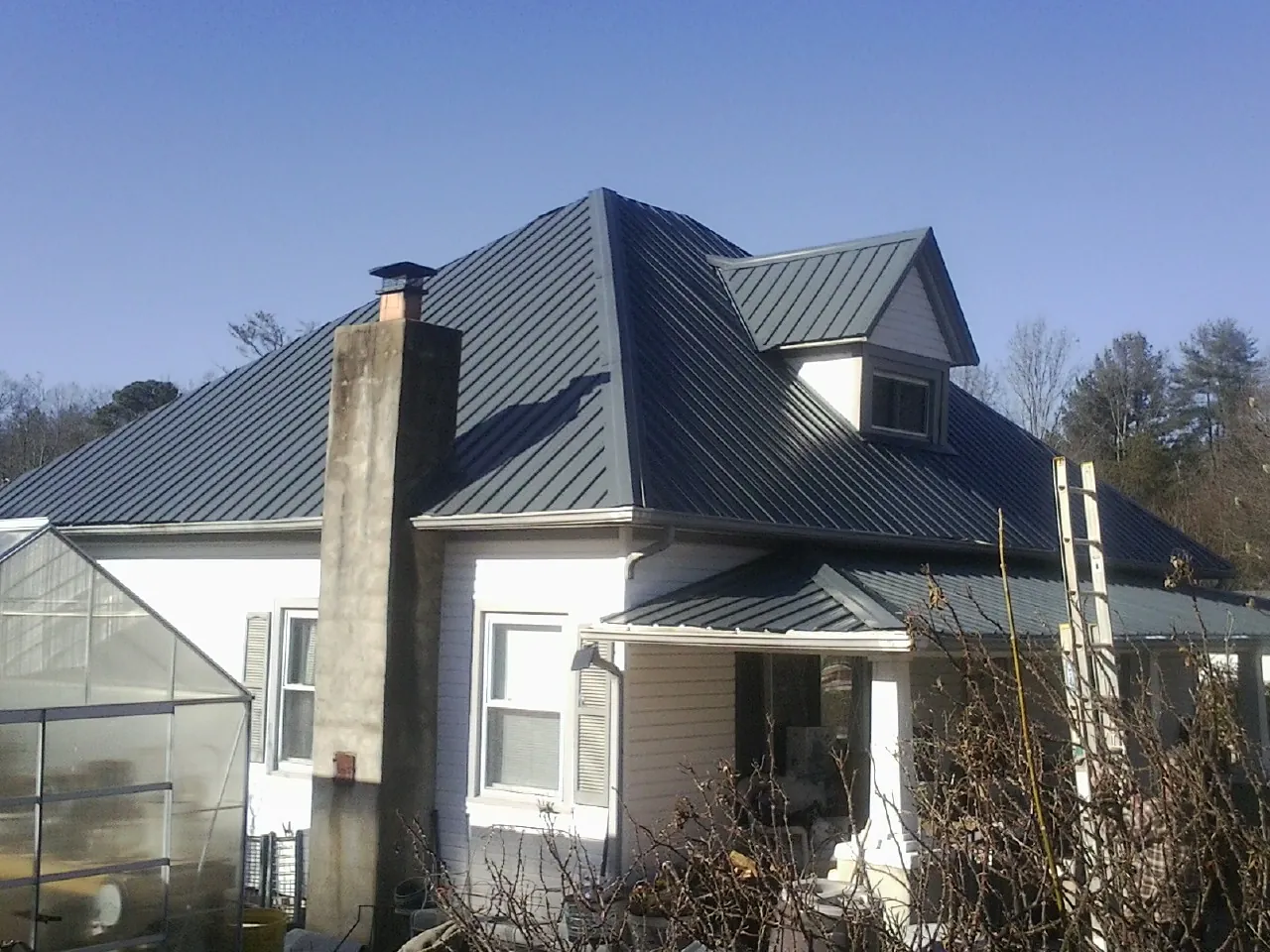 Dark blue standing seam metal roof on a white farmhouse with dormer — Slate & Tile Roof Repair by Roofing Brothers in Sandston