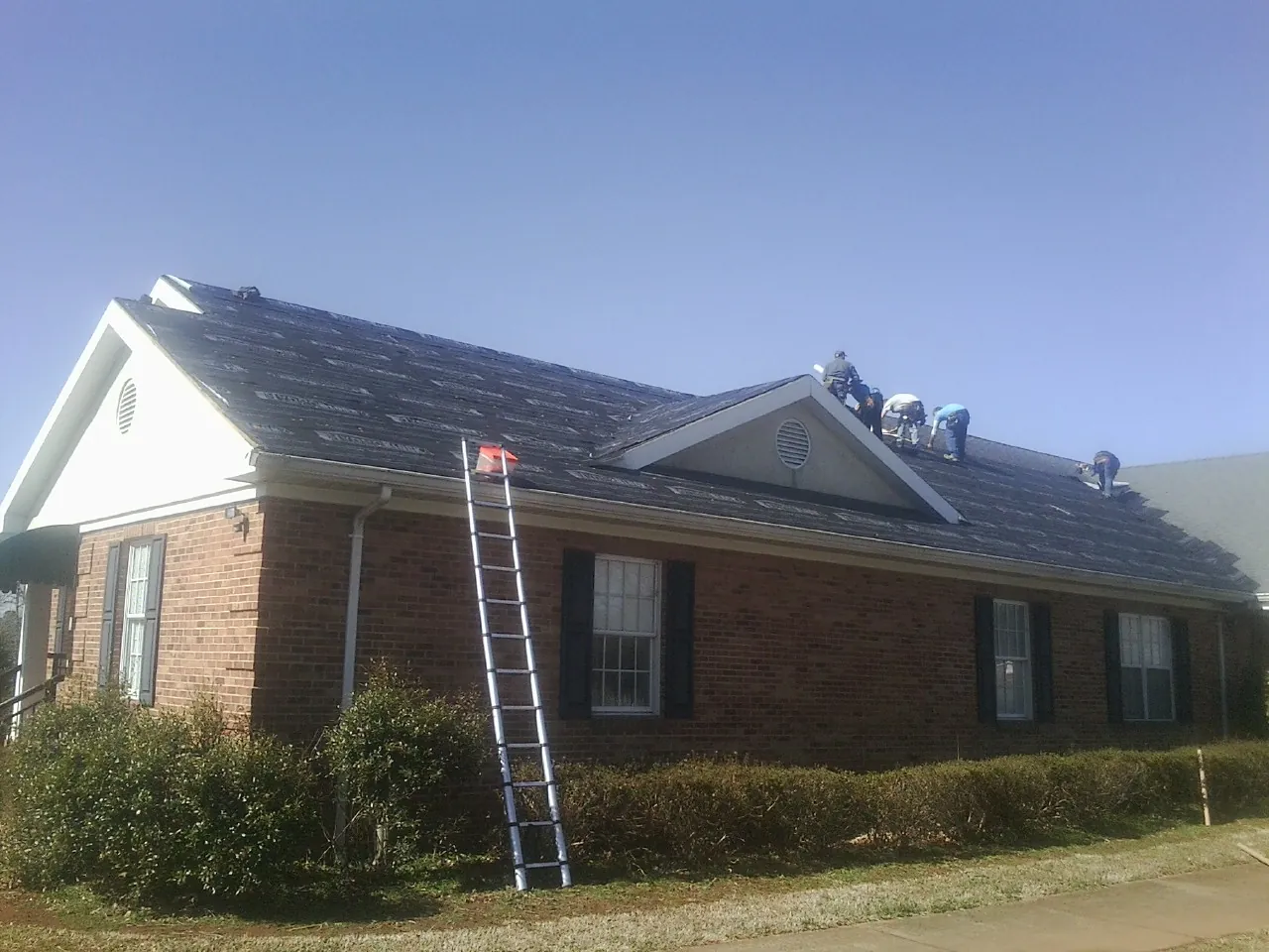 Crew tearing shingles off a brick ranch roof with a ladder set — Emergency Roof Repair work by our crew in Sandston