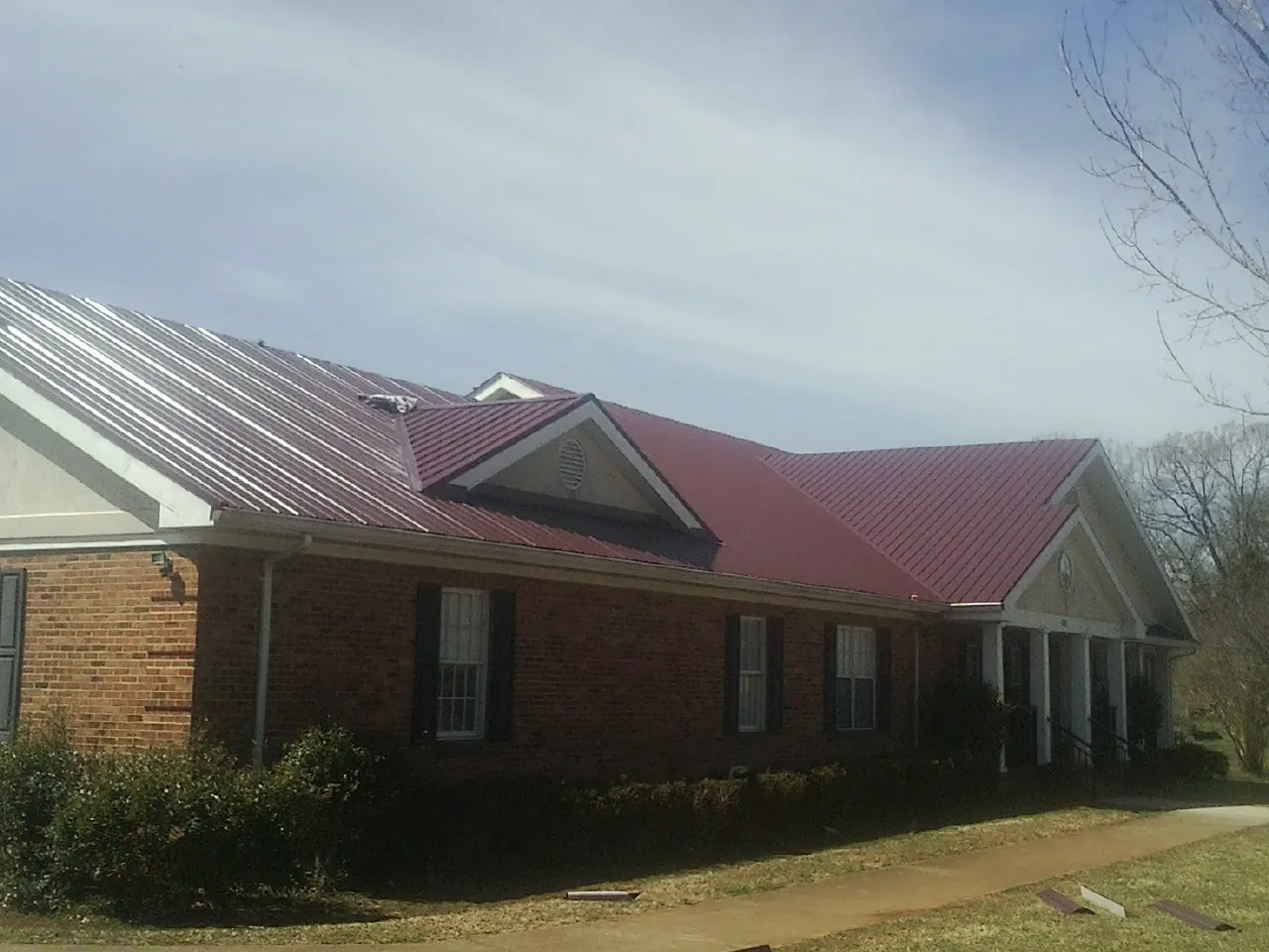 Red metal roof with gabled entries on a long brick building, from a Hail Damage Roof Repair job in Sandston